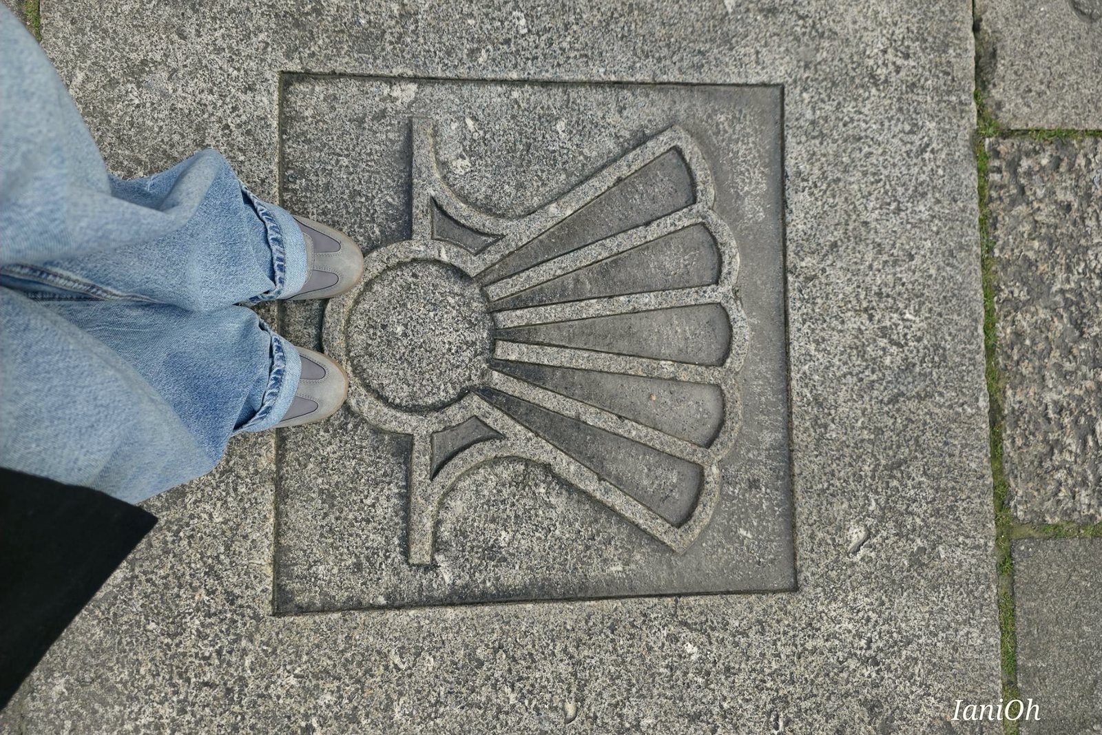 Pies junto a una concha del Camino de Santiago grabada en piedra